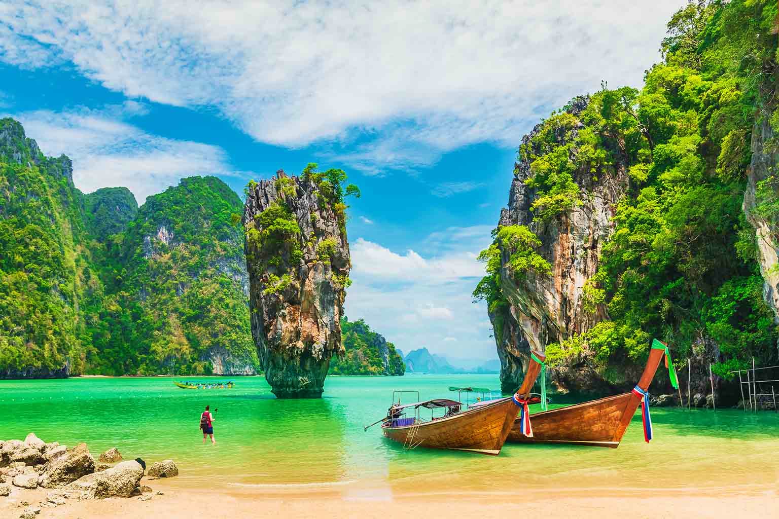 Traditional wooden longtail boats anchored in turquoise water near iconic limestone cliffs at James Bond Island, Thailand